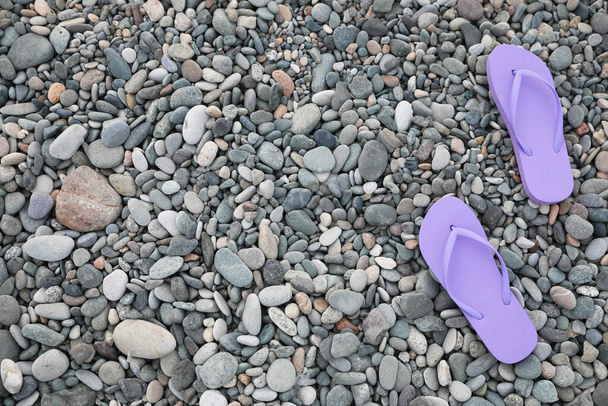 Stylish violet flip flops on pebble seashore, top view. Space for text - Foto, afbeelding