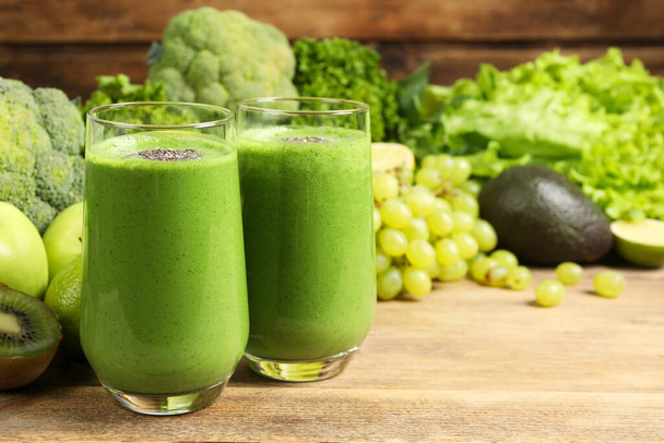 Glasses of fresh green smoothie and ingredients on wooden table, space for text - Фото, зображення
