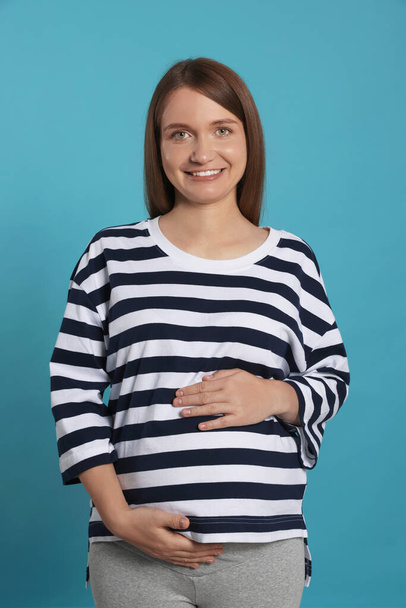Happy young pregnant woman on light blue background - Foto, Imagen