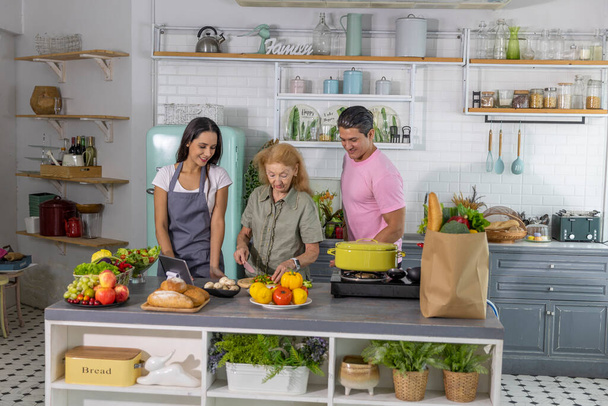 Fiatal pár dolgozik nagymama, hogy vegyenek online főzőtanfolyam és készítsen ételt otthon. A boldog család egészséges ételekkel készíti a reggelit. - Fotó, kép