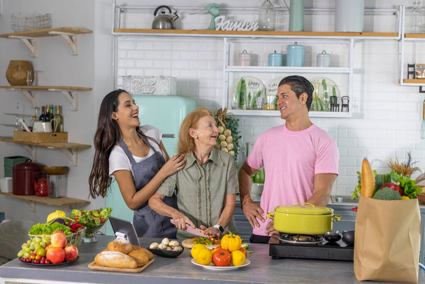Mladý pár pracuje s babičkou, aby se on-line kurz vaření a připravit jídlo doma. Šťastná rodina vaří snídani se zdravým jídlem společně - Fotografie, Obrázek