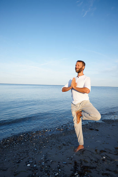 Equilibrato sulla spiaggia. Colpo pieno di un bell'uomo maturo che fa yoga sulla spiaggia - Foto, immagini