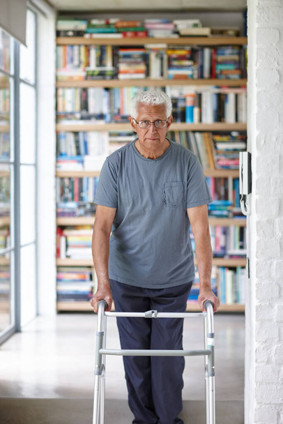 En movimiento con la ayuda de un caminante. Retrato de un hombre mayor de pie con la ayuda de un caminante en el interior - Foto, imagen