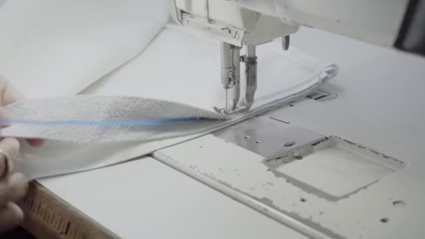 Ompelija työpajassa ompelee tuotteen, joka on valmistettu valkoisesta aidosta nahasta, jossa on valkoiset langat ompelukoneessa - Materiaali, video
