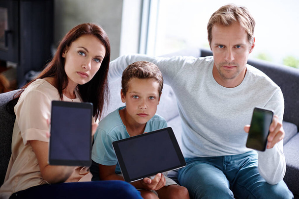 A tecnologia está a atrapalhar o tempo da família. Retrato de uma família olhando sério como eles seguram seus dispositivos digitais - Foto, Imagem