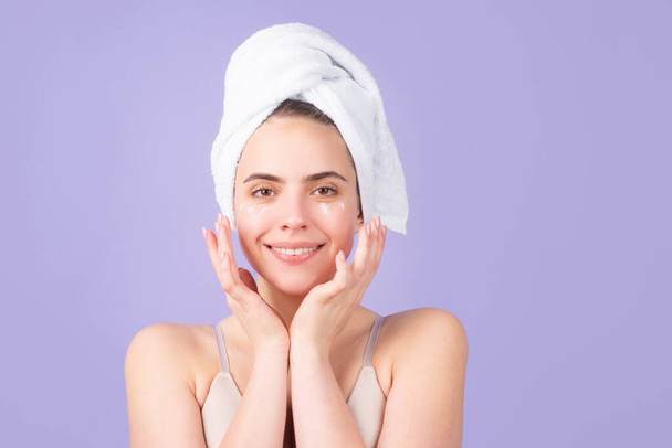 Beautiful woman with clean fresh skin. Girl beauty. Facial treatment, cosmetology, beauty and spa. Young girl with a towel on head apply a cleansing mask cream on her face - 写真・画像