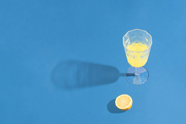 黄色のレモンドリンクとの最小限のコントラストのアイデア青の背景に。ミニマルなカラフルなパーティーコンセプト. - 写真・画像