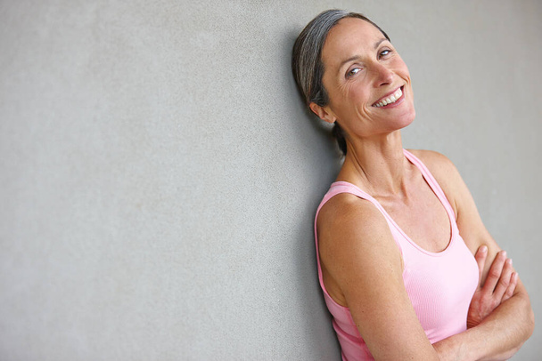 Feeling great. Portrait of an attractive mature woman in gymwear leaning against a gray wall - Foto, Imagem