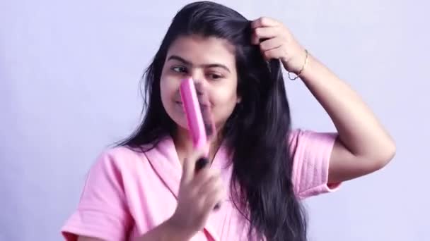 Docela šťastná indická žena kartáčování vlasy na sobě župan na bílém pozadí a ukazuje žádný pád vlasů - Záběry, video