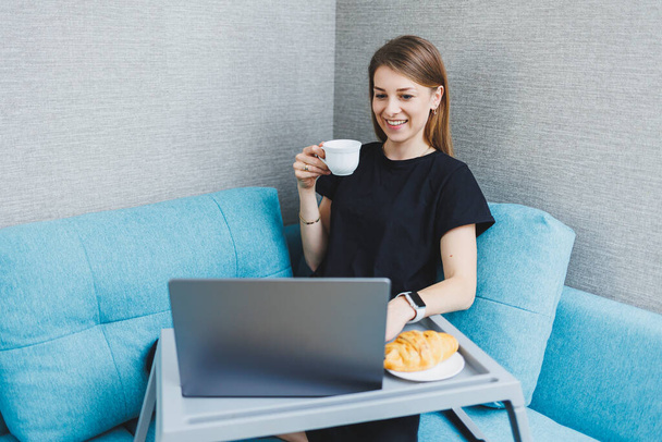 Genç bir kadın evdeki koltukta otururken dizüstü bilgisayarla sabah kahvesinden zevk alıyor. Çekici, mutlu bir kız öğrenci bilgisayarda yazı yazıyor. İnternette eğleniyor ya da kanepede dinlenirken arkadaşlarıyla sohbet ediyor. - Fotoğraf, Görsel