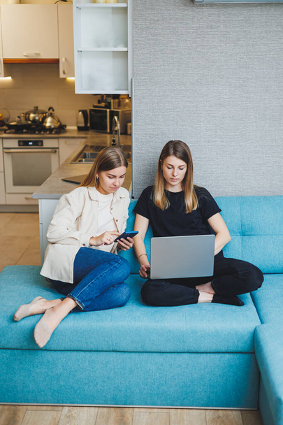 Two beautiful young women using laptop watching movie sitting on sofa at home, two female friends sitting on sofa at home in living room. - Foto, Bild