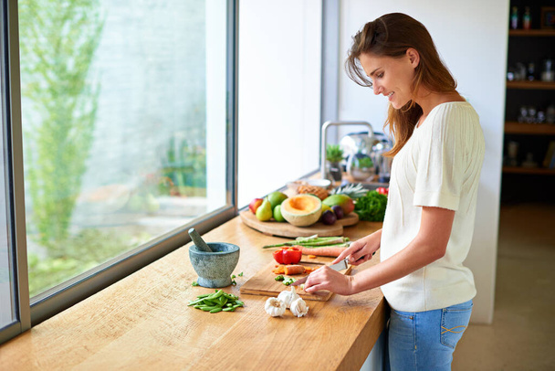 Het recept komt samen. een aantrekkelijke jonge vrouw hakken groenten in een keuken - Foto, afbeelding