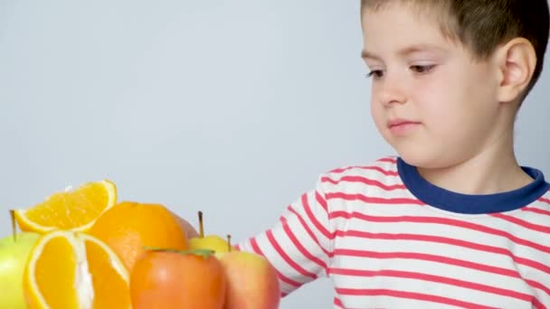 Pieni poika ja hedelmät - lapsi katsoo appelsiineja ja persimmonseja, näyttää kielensä, rypistää. - Materiaali, video