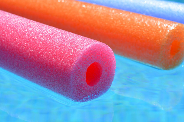Летние вибрации, красочные розовые, оранжевые и голубые полиэтиленовые лапши плавающие в бассейне - Фото, изображение