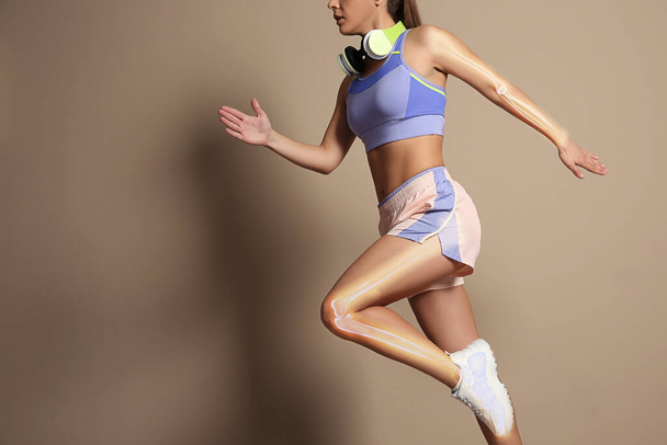 Digital composite of highlighted bones and woman in sportswear with headphones running on beige background - Foto, Imagen