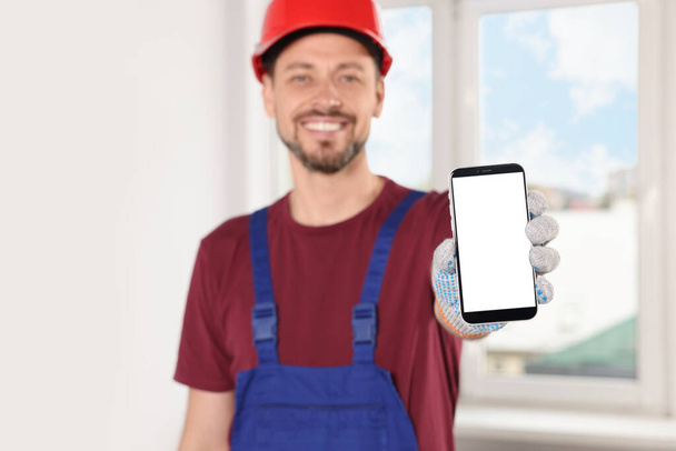 Professional repairman in uniform with phone indoors, focus on hand - Φωτογραφία, εικόνα