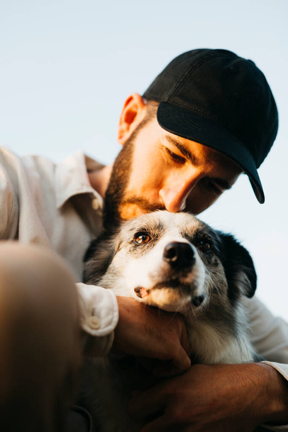 Portrait of a young bearded man wearing a black cap, with his dog, at countryside - Foto, Imagem