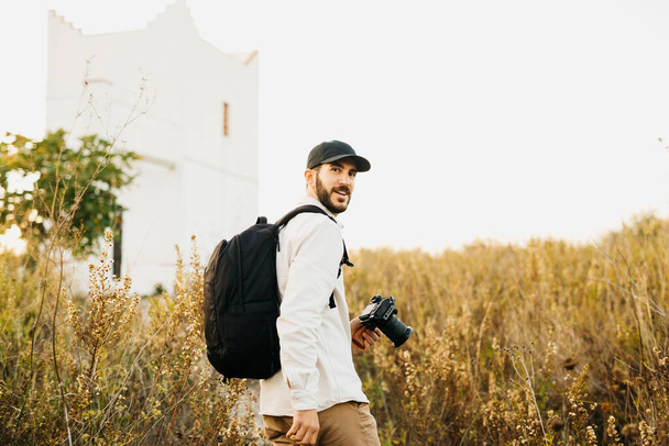 Siyah şapkalı genç bir sakallı adamın portresi, kırsal kesimde dijital kamerasıyla. - Fotoğraf, Görsel