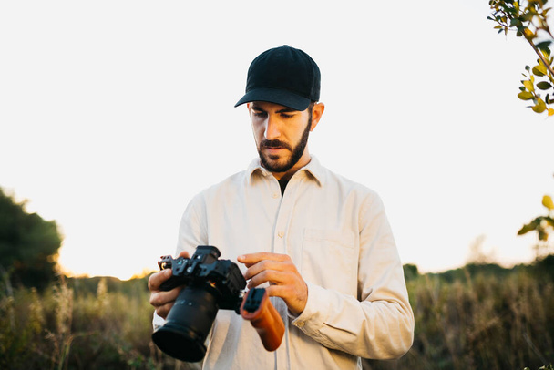 Porträt eines jungen bärtigen Mannes mit schwarzer Mütze und Digitalkamera auf dem Land - Foto, Bild