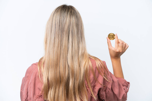 Young caucasian woman holding a Bitcoin isolated on white background in back position - Foto, imagen