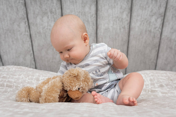 Close up of inquisitive cute baby European boy touching soft bear toy profile portrait sitting on sofa at home, pretty child playing in playroom - Photo, image