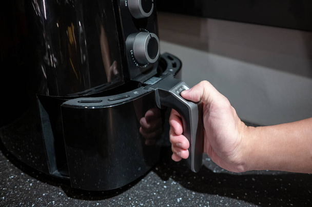 Mannelijke hand met een elektrische friteuse handvat in de keuken. Huishoudapparaat voor een gezonde kookstijl. - Foto, afbeelding