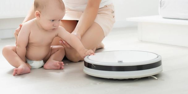 Little baby boy looks at the robotic vacuum cleaner at home - Fotografie, Obrázek