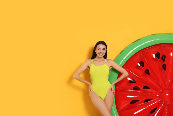 Young woman in stylish swimsuit near inflatable mattress against orange background. Space for text - Fotografie, Obrázek