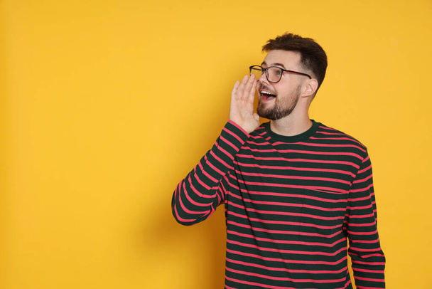 Handsome man in striped sweatshirt screaming on yellow background, space for text - Fotoğraf, Görsel
