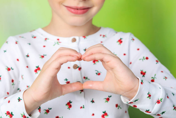 Little girl making heart with hands on blurred background, closeup - Foto, Bild