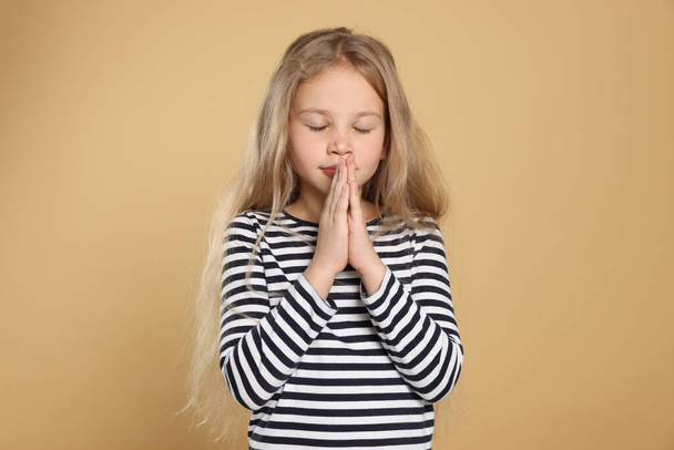 Girl with clasped hands praying on beige background - Фото, изображение