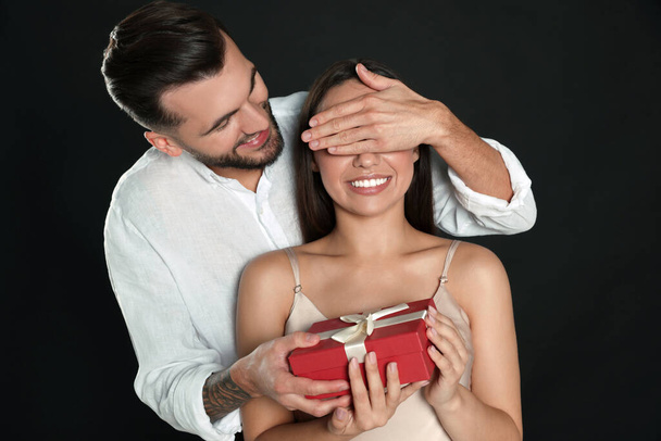 Man presenting gift to his girlfriend on black background - Foto, afbeelding