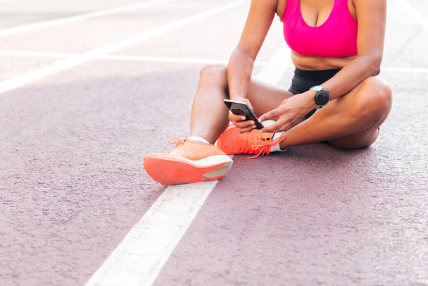 unrecognizable female athlete using her mobile phone sitting on the athletics track after her workout, concept of sport and healthy lifestyle, copy space for text - Fotoğraf, Görsel