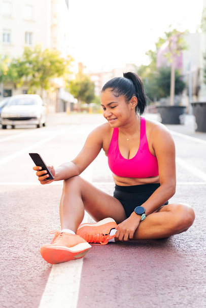 female athlete using her mobile phone sitting on the city athletics track after her workout, concept of sport and healthy life style, copy space for text - Fotó, kép