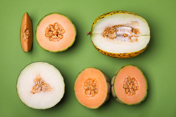 Cut different types of melons on green background, flat lay - Фото, изображение