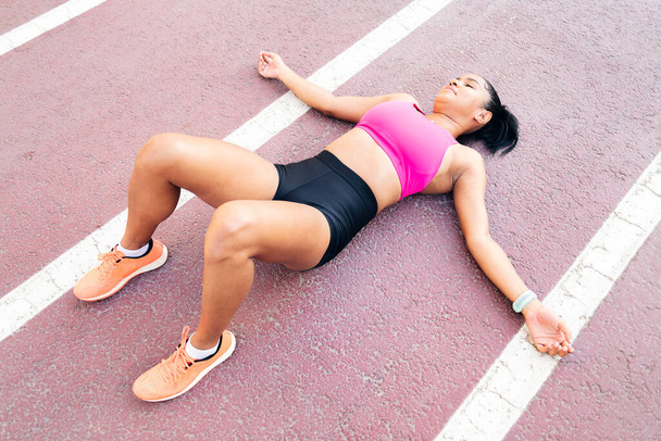female athlete in sportswear resting lying on the running track after her workout, concept of sport and healthy lifestyle, copy space for text - Photo, Image