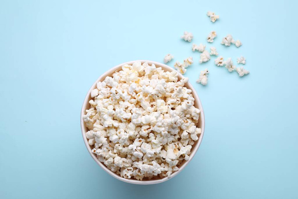 Paper bucket with delicious popcorn on light blue background, flat lay - Fotó, kép