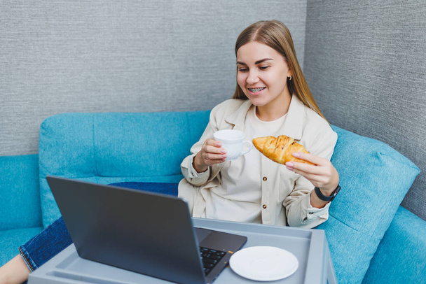 Young happy freelancer woman sitting on sofa working on project, watching movie on laptop, studying, blogging, relaxing and chatting online. High quality photo - Fotografie, Obrázek