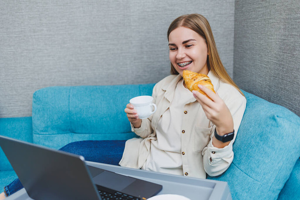 Усміхнена жінка використовує ноутбук, щоб перевірити новини електронної пошти в Інтернеті, сидячи на дивані, працюючи на комп'ютері, пишучи блог або переглядаючи вебінар, навчаючись вдома
 - Фото, зображення