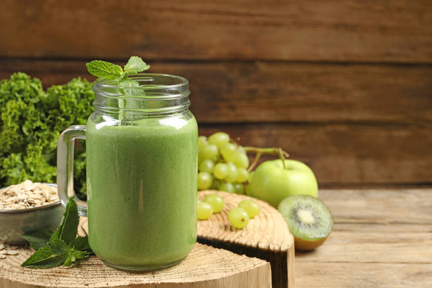 Mason jar of fresh green smoothie and ingredients on wooden table, space for text - Foto, imagen