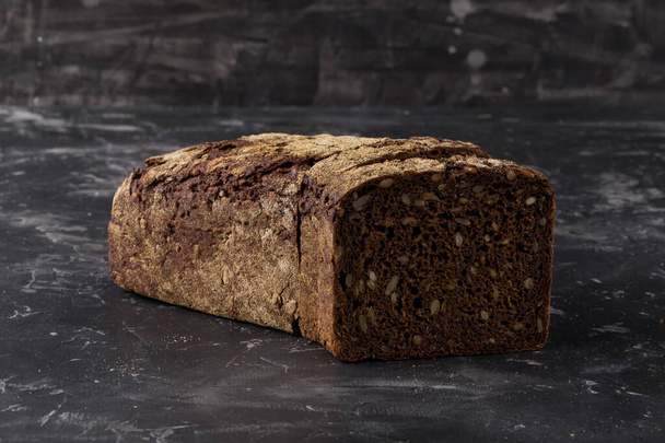 Черный хлеб с семенами на фоне темной доски - Фото, изображение