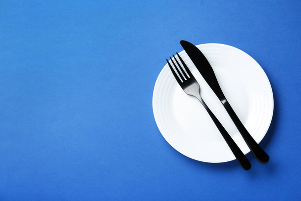 Assiette blanche propre avec couverts sur fond bleu, vue de dessus. Espace pour le texte - Photo, image
