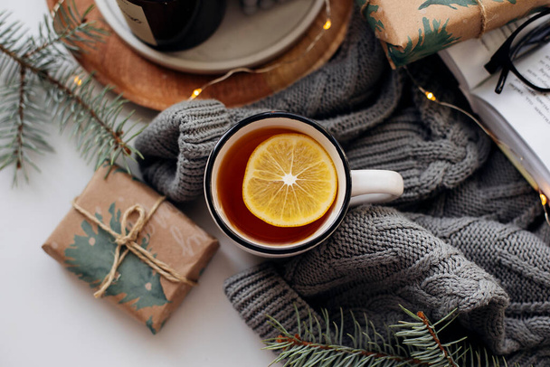 Cozy winter breakfast concept. Tea with lemon, candles, books and warm knitted sweater on white background. Top view - Photo, Image
