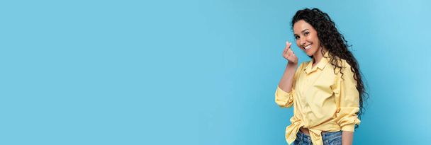 Wide horizontal banner with smiling young woman making mini heart finger gesture while standing isolated on blue background, extended shot of beautiful millennial lady showing like or love sign - Photo, Image