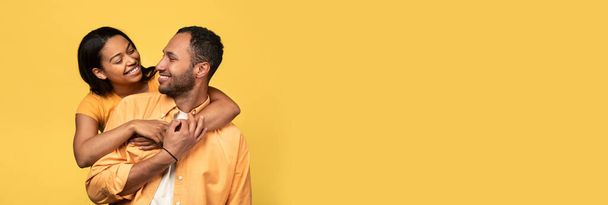 Długi baner poziomy z romantyczną czarną parą obejmującą żółte tło, szeroki kadr szczęśliwego młodego Afrykanina amerykańskiego mężczyzny i kobiety przytulających się i uśmiechających się do siebie, panorama z przestrzenią do kopiowania - Zdjęcie, obraz