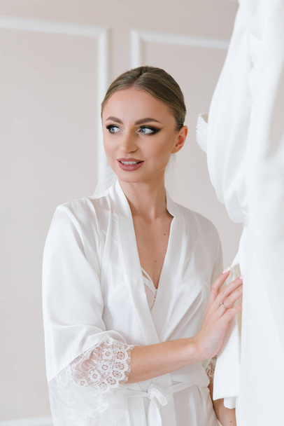 Fees for the wedding of a beautiful luxurious bride in a bathrobe with a wedding dress in a hotel, fashion portraits - Фото, изображение