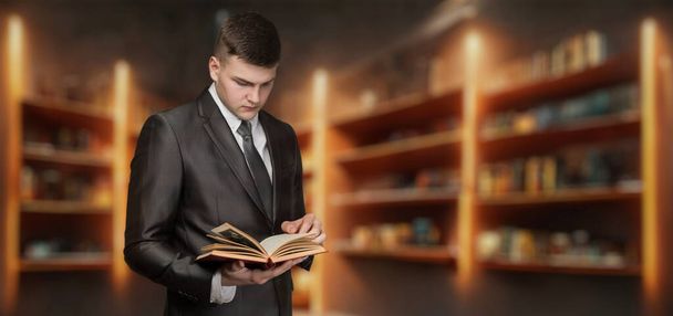 Jongeman in pak die een boek leest in de bibliotheek op een wazige achtergrond. - Foto, afbeelding