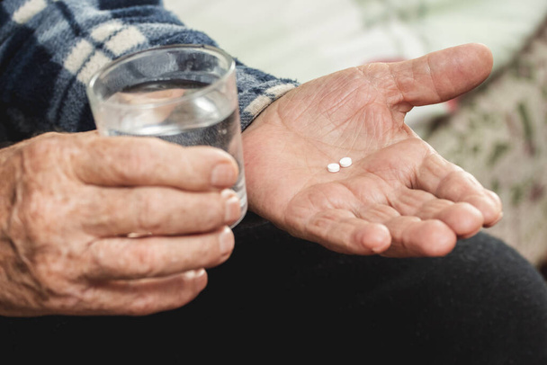 Un uomo anziano tiene in mano pillole e un bicchiere d'acqua. Prendendo pillole per trattare la malattia - Foto, immagini