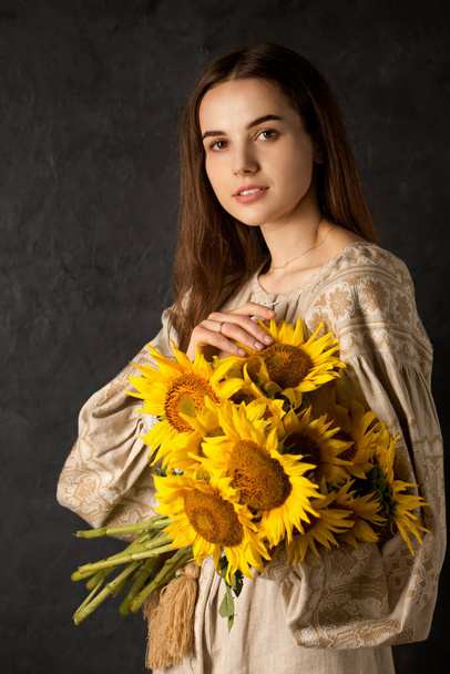 Ukrainian woman in a black embroidered dress with a bouquet of sunflowers on a dark background - Photo, Image