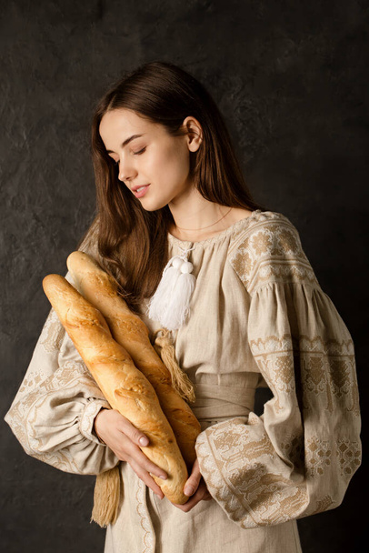 A Ukrainian woman in national clothes holds crispy baguettes in her hands - Zdjęcie, obraz